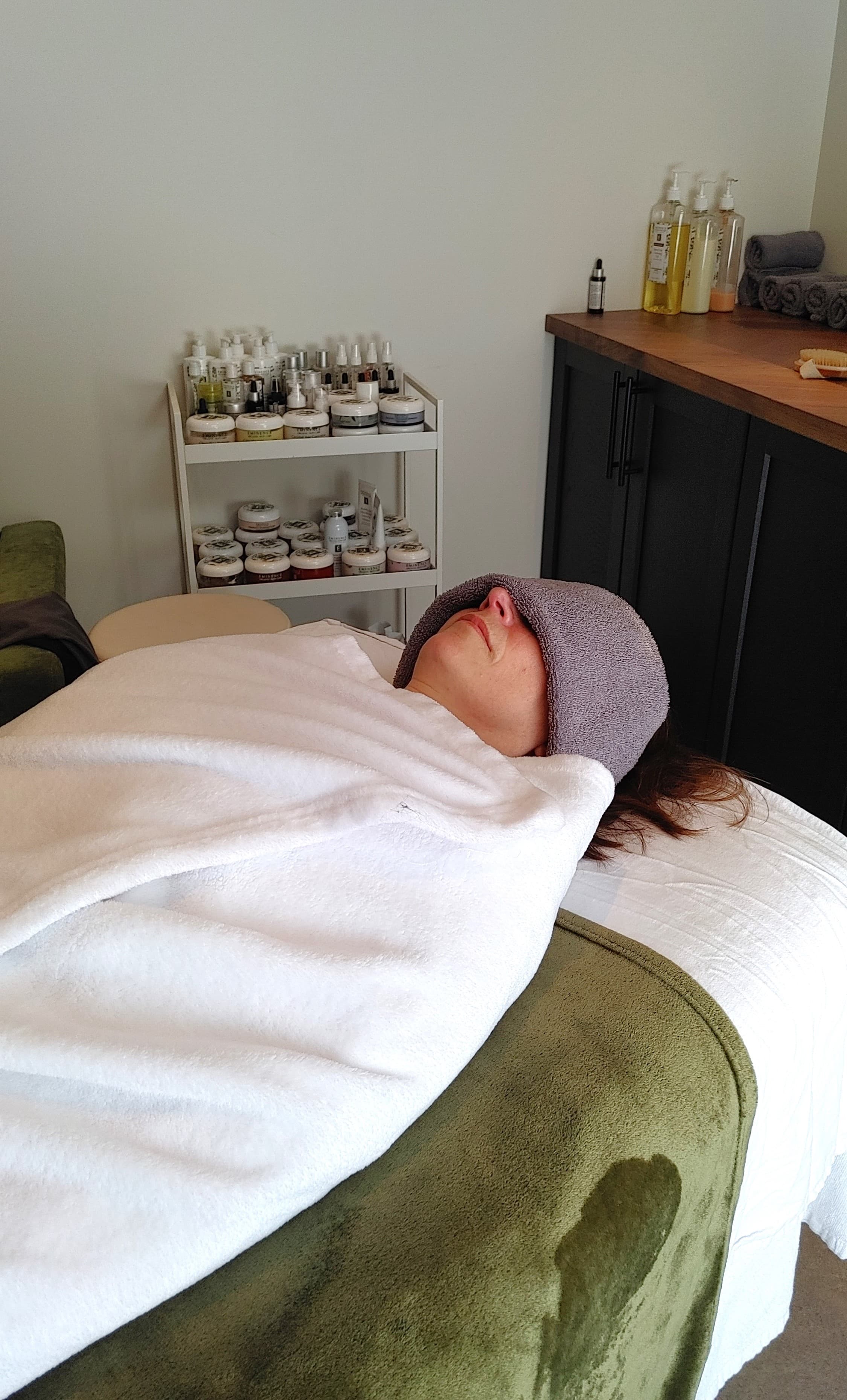 A woman laying on a massage table, wrapped in a cozy white blanket and a towel across her eyes