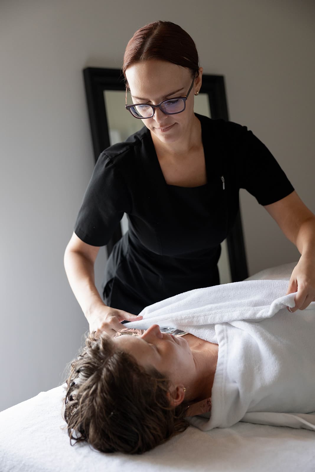 An esthetician applies sugar scrub to a client's arm on a massage table